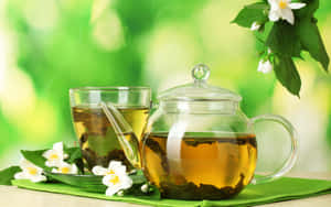 玻璃茶壺和杯子盛載茉莉花茶，配以新鮮花朵和葉子，置於綠色布上。 — MacBook Air M1 壁紙