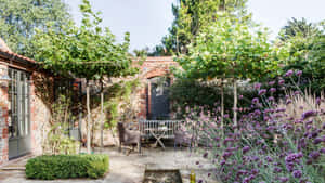 石頭庭院花園，種有薰衣草灌木和木桌椅子，位於綠樹下。 — 花園牆外 壁紙