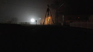 一個高大的骷髏身影站在霧夜場景中，背景有明亮的月亮和街燈。 — 暗色 壁紙