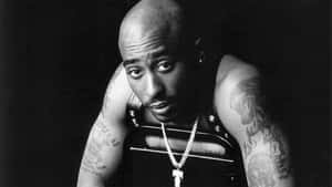Tupac Shakur 的黑白工作室肖像，帶有紋身和鏈條。