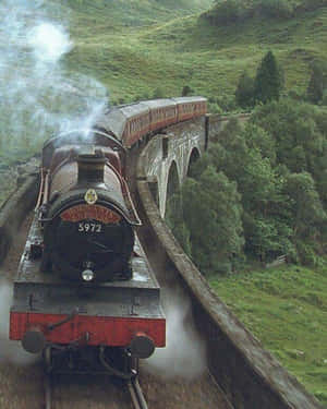Hogwarts Express 蒸汽火車在綠樹成蔭的山谷中穿越石橋。 — Apple Watch Ultra 壁紙