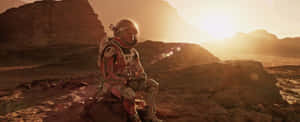 在荒蕪行星上金色日落時分，太空人坐在外星岩石上。 — 火星 GIF 壁紙