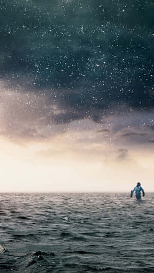 一名太空人在有雲的星空下，在海水裏行走。 — 銀河手機 壁紙