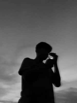 一個人在陰雲密佈的黃昏天空下點燃香煙的剪影。