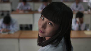 一名微笑的穿校服女孩在教室裡看著鏡頭。 — Netflix GIF 壁紙