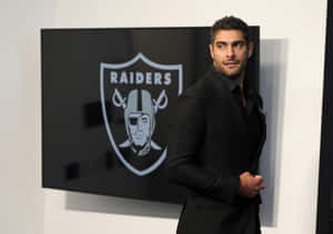 身穿黑色西裝的男子站在顯示Raiders標誌的屏幕旁 — 戰士 壁紙