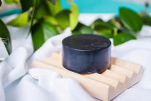 黑色肥皂放在木碟上，配綠葉和白布 — 3:2 壁紙