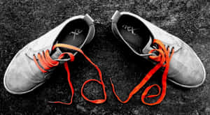 灰色運動鞋，橙色鞋帶在深色地面上拼出 love。 — 卡通鞋 壁紙