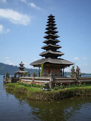 峇里島寺廟位於水上島嶼，背景有花朵和山脈 — 廟宇 壁紙