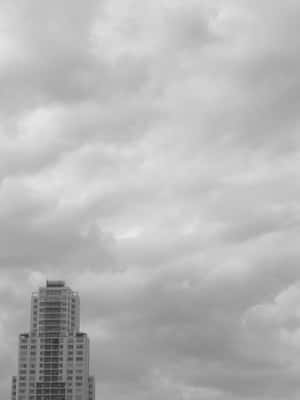 在沉重的雲層密布的天空下，黑白相間的摩天大樓高聳入雲。 — Kindle 壁紙