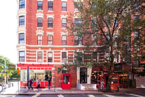 紅磚建築，帶有白色飾邊和地面層商店，位於陽光明媚的城市街道上。 — MacBook Air 13 壁紙