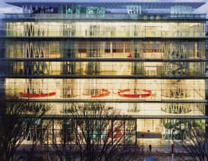 黃昏時亮燈的玻璃建築內部，透過窗戶可見紅色圓形座位。 — 黃昏 壁紙