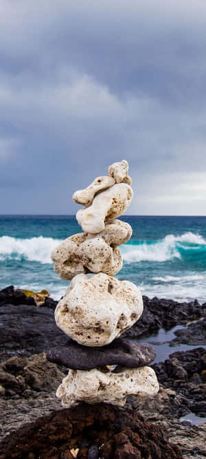 在岩石海灘上堆疊的珊瑚石，伴隨著拍打的波浪和暴風雨的天空。 — Motorola Edge 壁紙