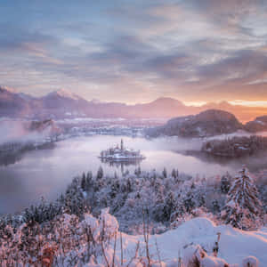 雪覆蓋的島嶼教堂，位於霧湖上，日出時分，背景有山脈 — iPad Pro 12.9 壁紙
