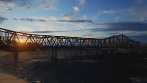 金色日落與雲層下，河流上的鋼製桁架橋 — 日落 壁紙