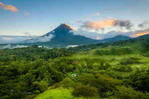 火山頂峰從雲層中浮現，下方是鬱鬱蔥蔥的綠色山丘，日出時分。 — 牙買加海灘 壁紙