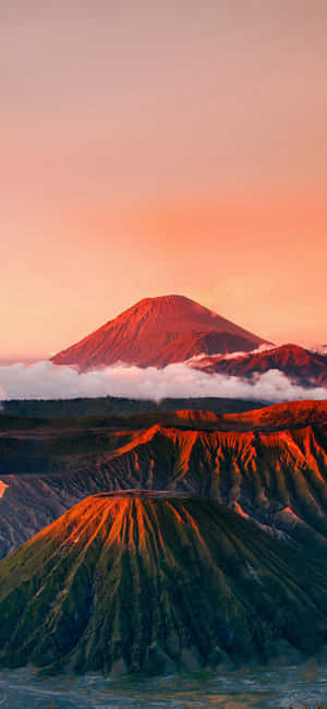 火山山脈沐浴在日落橙色光芒中，下方有雲層。 — Moto E 壁紙
