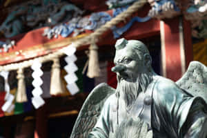 在一個有色彩繽紛的鳥居和紙垂的日本神社中的青銅有翼守護者雕像。 — 廟宇 壁紙