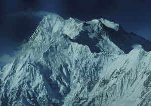 在深藍色天空下，一座雄偉的雪山山峰被雲霧環繞。