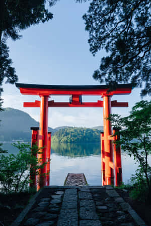 紅色鳥居俯瞰平靜的湖泊，周圍環繞著綠樹和山巒。 — 2:3 壁紙