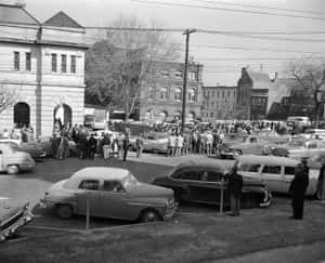 人群聚集在繁忙的1950年代街道上的經典汽車周圍。 — 復古gif 壁紙