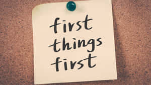 便利貼上寫有手寫文字 first things first，釘在軟木板上。 — 1280x720 壁紙