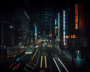 霓虹燈城市街道夜景，帶有流動的車燈軌跡和高聳的建築物。 — 夜景城市 壁紙