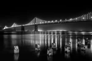 燈光吊橋的夜景，水面倒影及前景木樁。 — MacBook Pro M4 壁紙
