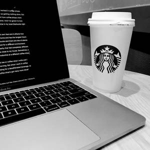 星巴克咖啡杯旁邊放著一部MacBook Pro在木桌上。 — 黑白 壁紙