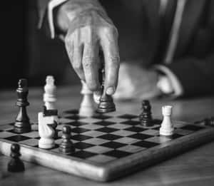 對弈中，一隻手在木製棋盤上移動一枚棋子。 — 國際象棋 壁紙