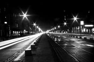 夜晚的城市街道，濕漉漉的路面上有發光的街燈和拖曳的車燈。 — MacBook Pro 14 壁紙