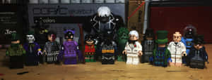 LEGO蝙蝠俠反派在木桌上擺姿勢，背後有美術用品。 — 超寬螢幕 壁紙