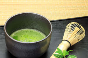 陶瓷碗中的抹茶，配以竹筅和新鮮茶葉，置於黑色托盤上。 — 青綠色 GIF 壁紙
