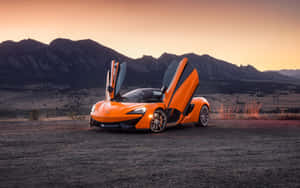 橙色McLaren跑車在夕陽下的山區沙漠中打開車門。 — 麥拿侖 GIF 壁紙