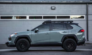鼠尾草綠色豐田RAV4，配黑色配件，停在灰色磚砌建築前。 — 低調 壁紙