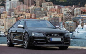 黑色Audi S8房車停泊在遊艇碼頭，後面是城市建築。 — Steam Deck OLED 壁紙