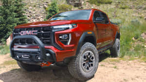 紅色GMC Canyon AT4皮卡車停泊在岩石自然環境中的泥路上。 — 16:9 壁紙