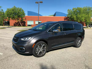 深灰色 Chrysler Pacifica 小型貨車停泊在磚砌建築物附近的陽光停車場。