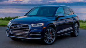 深藍色 Audi SQ5 SUV 停泊在黃昏時分湖邊，遠處有山巒。 — 奧迪 GIF 壁紙