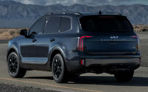 深藍色Kia Telluride SUV停泊在沙漠公路上，後面有山脈。 — MacBook Air M1 壁紙