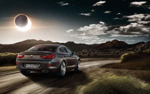 灰色BMW 6系在日食期間於沙漠公路上飛馳，背後有山脈。 — Steam Deck OLED 壁紙