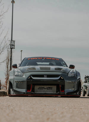灰色日產GT-R賽車，帶有紅色飾邊，停泊在陰天下的瀝青路面上。 — 汽車 壁紙
