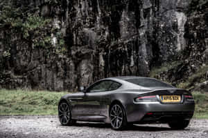 啞光灰色 Aston Martin 跑車停泊在佈滿青苔的懸崖旁邊。 — Surface Pro 壁紙