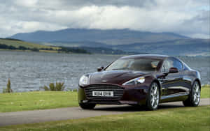 棗紅色Aston Martin停泊在湖邊，背景有山。 — Steam Deck 壁紙