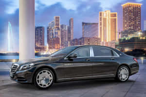 豪華 Mercedes-Maybach S-Class 轎車停泊在黃昏時分發光的城市天際線前。 — 酷車 壁紙