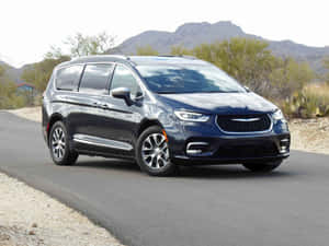 深藍色 Chrysler Pacifica 小型貨車在沙漠公路上，背景有山脈和仙人掌。