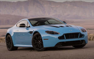 淺藍色 Aston Martin 跑車停泊在沙漠公路上，背景有山脈和日落。 — Steam Deck 壁紙