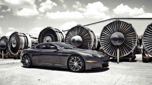 灰色 Aston Martin 跑車停泊在巨型噴射引擎旁。 — 黑白 壁紙