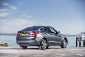 在清澈藍天下，灰色BMW X4 SUV停泊在海邊碼頭上。 — Surface Pro 壁紙