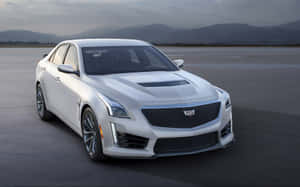 白色Cadillac CTS-V運動轎車在開闊混凝土上，以山巒為背景。 — MacBook Pro M1 壁紙